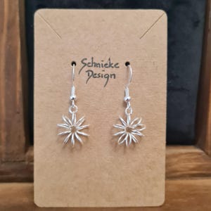 Könnte beinhalten: Silberne Ohrringe mit einem Blumenmuster. Die Ohrringe befinden sich auf einer braunen Karte mit dem Text "Schnicke Design".