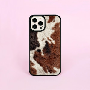 May include: A smartphone case with a black border and a cowhide pattern. The case features a brown, white, and black spotted design, mimicking the look of cow fur. The case has a glossy finish and is designed to fit a smartphone.