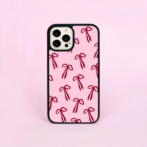 May include: A pink phone case with a black border featuring a pattern of red bows. The case is designed to fit a smartphone and has cutouts for the camera and buttons. The bows are evenly spaced across the surface.