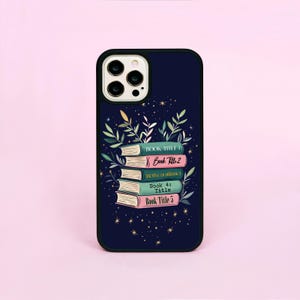 May include: A black phone case featuring a stack of books and stars on a dark blue background. The books have titles that read "Book Title 1", "Book Title 2", "The Title of Book 3", "Book 4: Title", and "Book Title 5".
