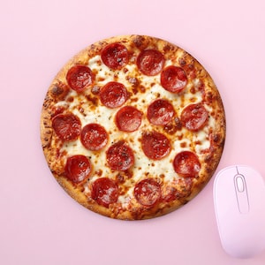 May include: A round pepperoni pizza with a golden crust and melted cheese. The pizza is topped with red pepperoni slices. A pink computer mouse sits beside the pizza on a pink background.