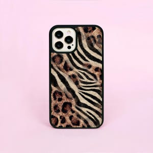 Könnte beinhalten: Eine schwarze Handyhülle mit einem gemischten Tiermuster. Das Design kombiniert Zebrastreifen und Leopardenflecken in Braun-, Beige- und Schwarztönen. Die Hülle hat einen schwarzen Rand und einen Kameraausschnitt.