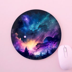 May include: Circular mouse mat with a watercolour depiction of a night sky filled with stars. The design uses blues, purples, and pinks, with trees silhouetted at the bottom. A white computer mouse is positioned beside the mouse mat.