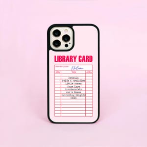 May include: A black phone case with a pink background. The case displays a pink library card design with the text "LIBRARY CARD" and the borrower's name "Helena". The card lists book titles such as "Dracula" and "Pride & Prejudice."