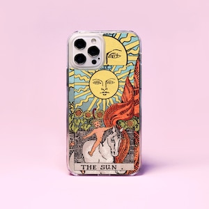 May include: A clear phone case featuring a colourful tarot card design. The card shows a sun with a face, a child riding a white horse, and sunflowers. The text "THE SUN." is printed at the bottom of the card.