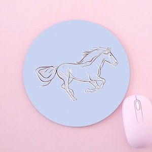 May include: A round, light blue mouse mat featuring a dark brown line art illustration of a galloping horse in the centre, positioned next to a light pink computer mouse on a matching light pink surface.