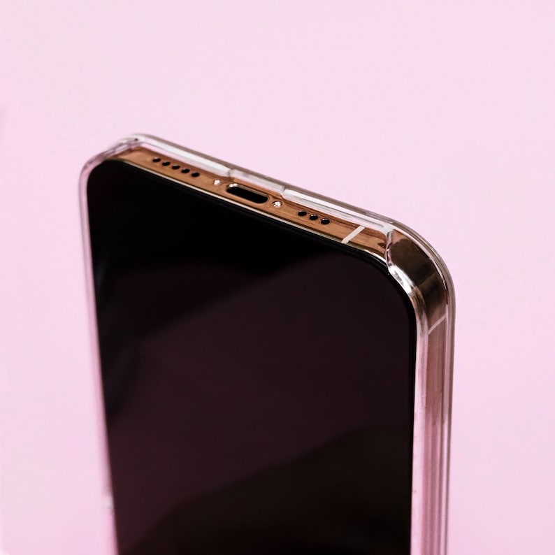 May include: A close-up of a black smartphone in a clear case. The phone is on a pink background.