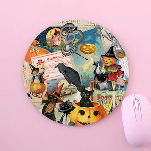 May include: Circular Halloween mouse mat with a collage of vintage illustrations. Features pumpkins, black cats, witches, and the text "QUICKSILVER POISON". The mouse mat is on a pink surface next to a pink computer mouse.