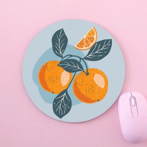 Puede incluir: Un ratón redondo azul con un diseño de naranjas y hojas. Las naranjas son de color naranja claro con un centro naranja más oscuro. Las hojas son de color verde oscuro.