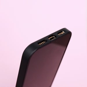 May include: Close-up of the top edge of a black phone case with gold-colored ports.