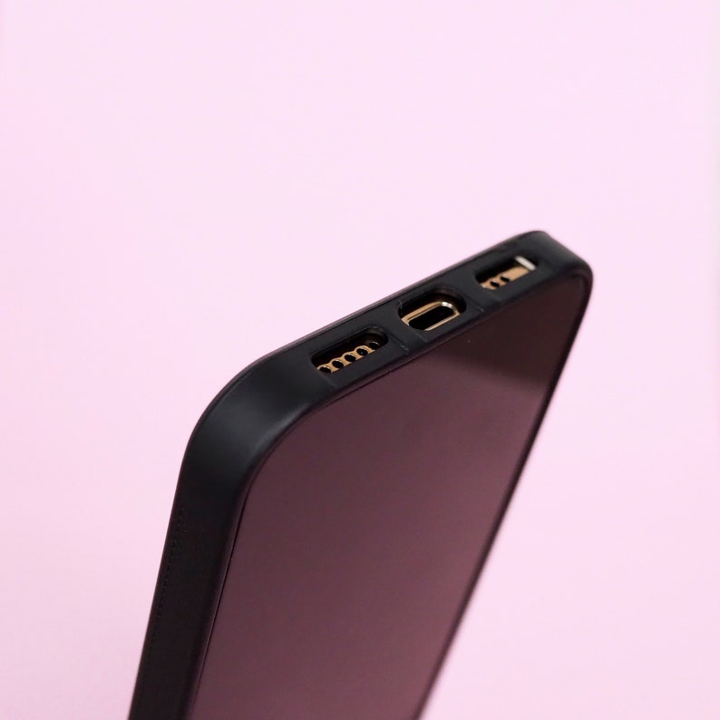 May include: Close-up of the top edge of a black phone case with gold-colored ports.