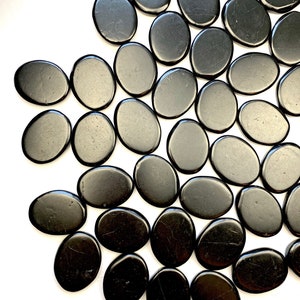 May include: A collection of smooth, black oval-shaped stones. The stones are arranged in a semi-circle pattern on a white background.