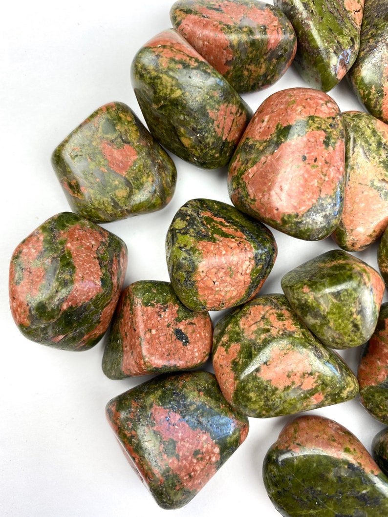 May include: A collection of tumbled green and red jasper stones. The stones are smooth and polished, with a variety of patterns and colors.