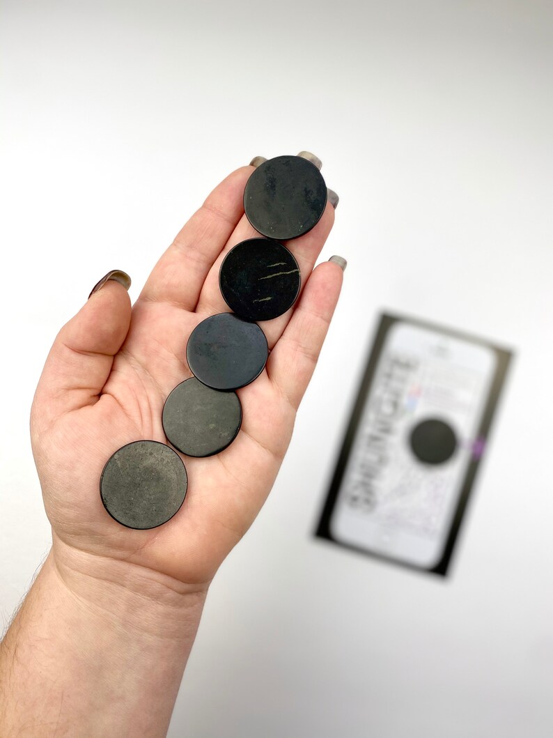 May include: Five black round smooth stones, also known as "worry stones", are held in a hand. The stones are approximately 1 inch in diameter.