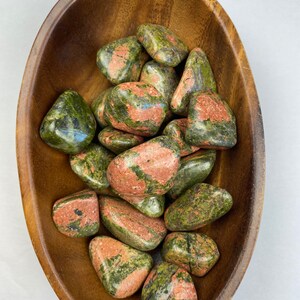 May include: A bowl of green and pink tumbled stones. The stones are smooth and polished, and they have a variety of shapes and sizes.