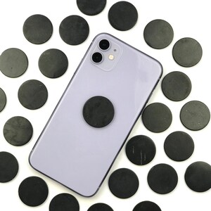 May include: A purple smartphone with a black phone grip and a black camera lens. The phone is surrounded by 20 black round discs.