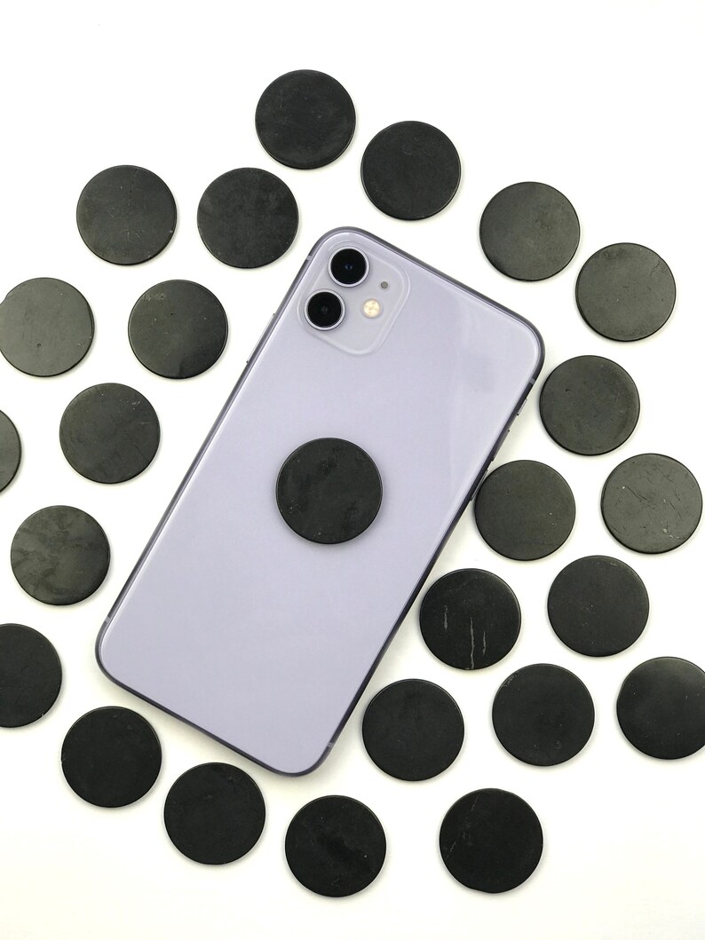 May include: A purple smartphone with a black phone grip and a black camera lens. The phone is surrounded by 20 black round discs.