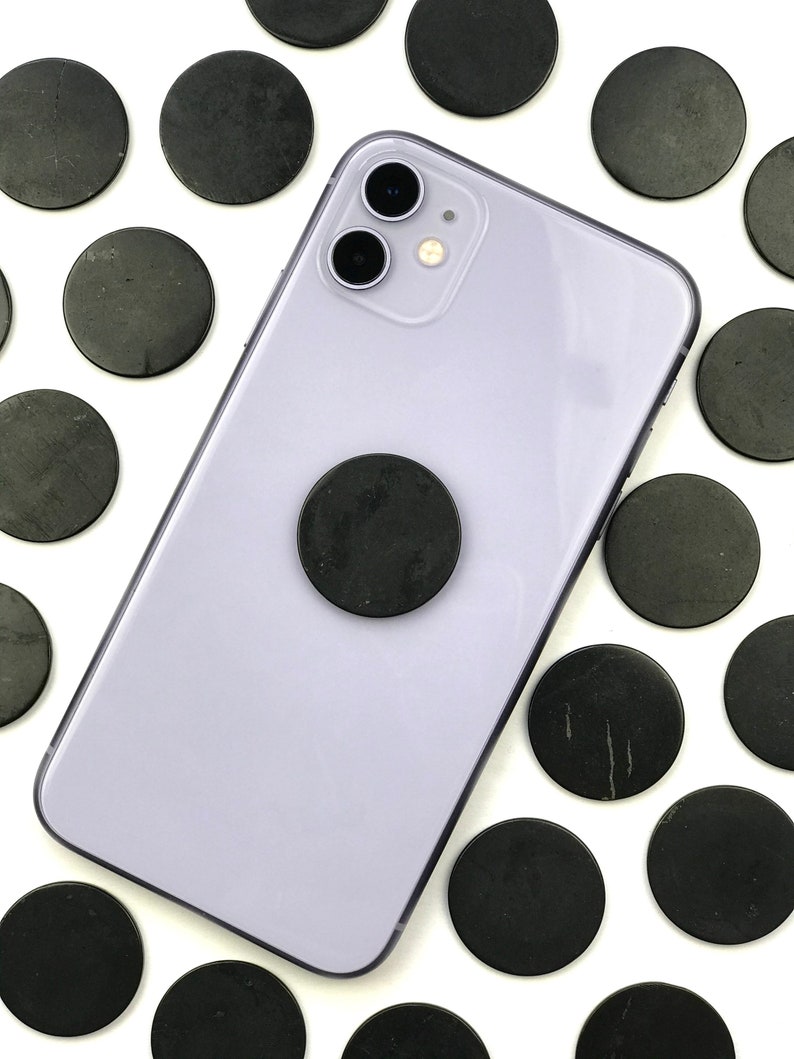 May include: A purple smartphone with a black phone grip and a black camera lens. The phone is surrounded by black round stones on a white background.