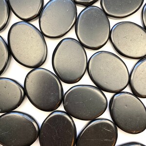May include: A collection of smooth, black oval-shaped stones. The stones are arranged in a random pattern on a white background.