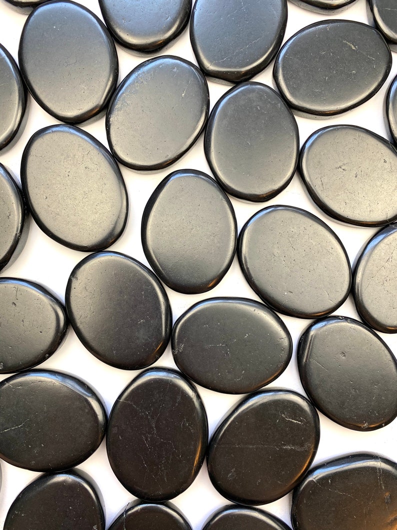 May include: A collection of smooth, black oval-shaped stones. The stones are arranged in a random pattern on a white background.
