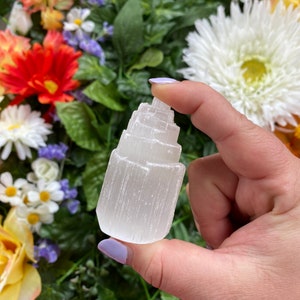 May include: A white selenite crystal tower with a layered, pointed top. The crystal is smooth and has a natural, raw texture.