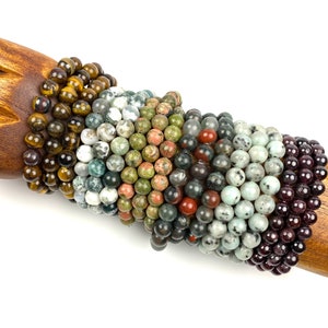 May include: A stack of eight bracelets made with various semi-precious stones, including tiger's eye, green aventurine, red jasper, and black obsidian.
