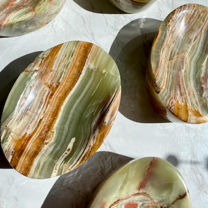 May include: Four green, brown, and white oval-shaped onyx bowls. The bowls are made of natural stone and have a smooth, polished finish.