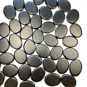 May include: A collection of smooth, black oval-shaped stones. The stones are arranged in a random pattern on a white surface.