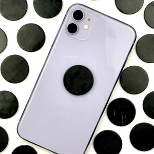 May include: A purple smartphone with a black phone grip and a black camera lens. The phone is surrounded by black round stones.