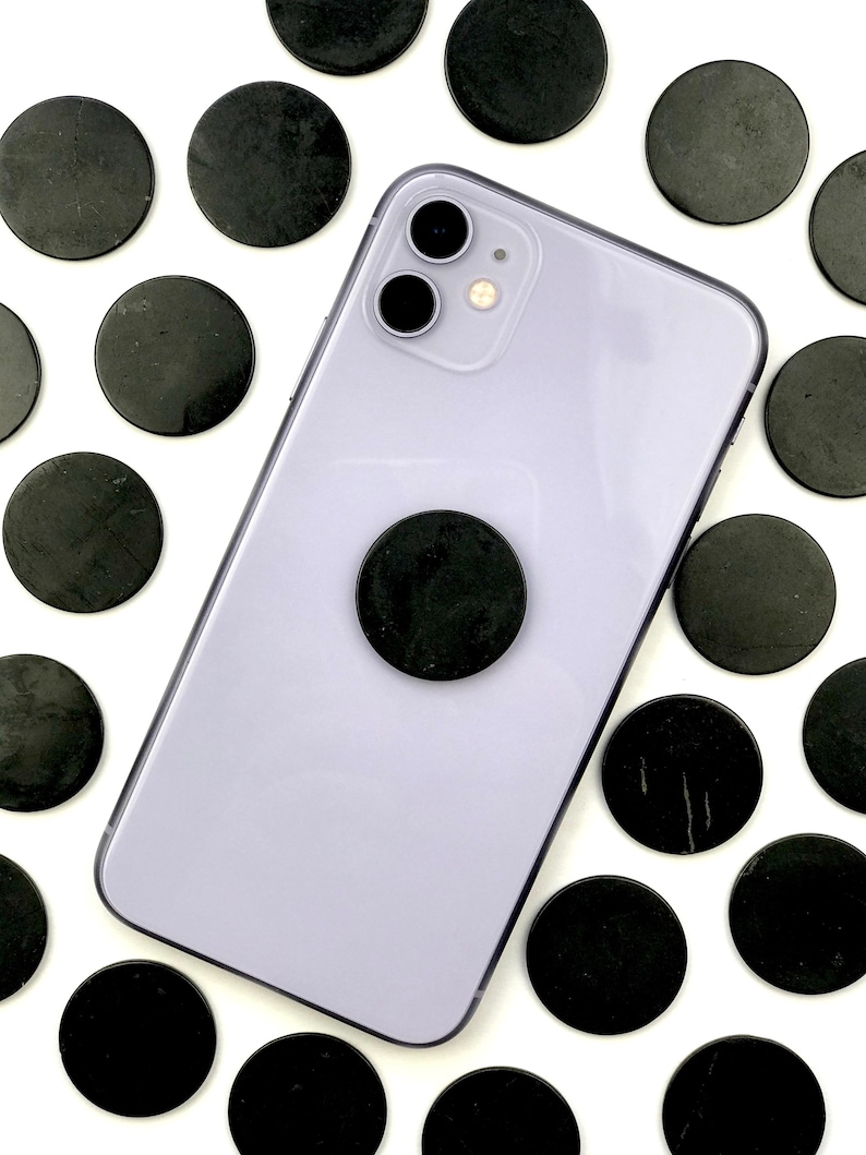 May include: A purple smartphone with a black phone grip and a black camera lens. The phone is surrounded by black round stones.