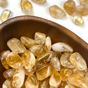 Puede incluir: Un cuenco lleno de piedras de citrino pulidas. Las piedras son de color amarillo claro a medio y tienen un acabado liso y pulido.