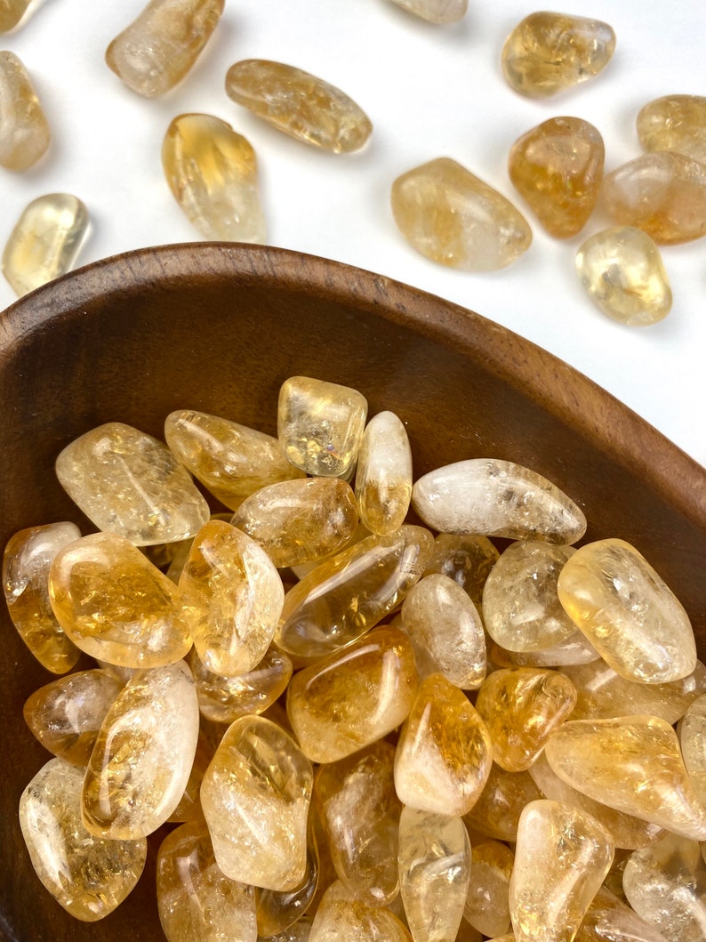 Puede incluir: Un cuenco lleno de piedras de citrino pulidas. Las piedras son de color amarillo claro a medio y tienen un acabado liso y pulido.