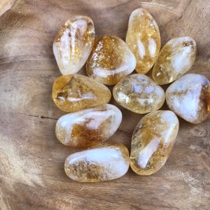 Puede incluir: Una colecci&oacute;n de piedras de citrino pulidas, cada una con una forma y un tama&ntilde;o &uacute;nicos. Las piedras son de color amarillo claro a medio y tienen una apariencia transl&uacute;cida.