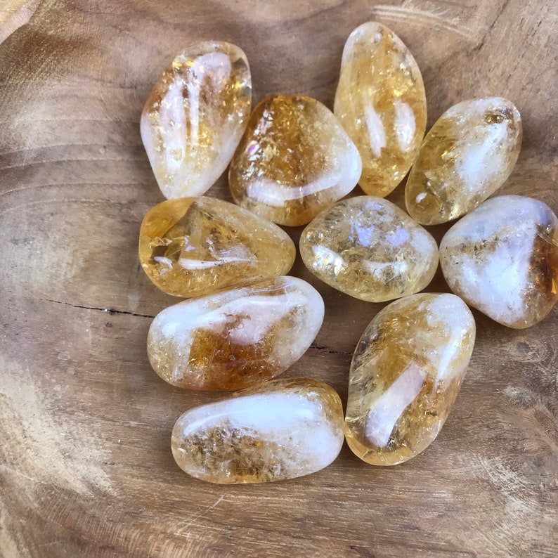Puede incluir: Una colecci&oacute;n de piedras de citrino pulidas, cada una con una forma y un tama&ntilde;o &uacute;nicos. Las piedras son de color amarillo claro a medio y tienen una apariencia transl&uacute;cida.