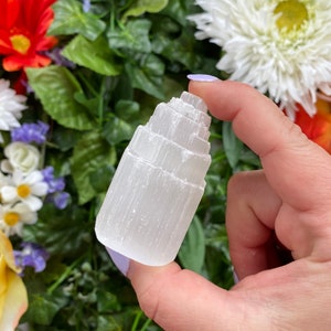 May include: White selenite crystal tower with a layered, stepped design. The crystal is smooth and polished, with a translucent white color.