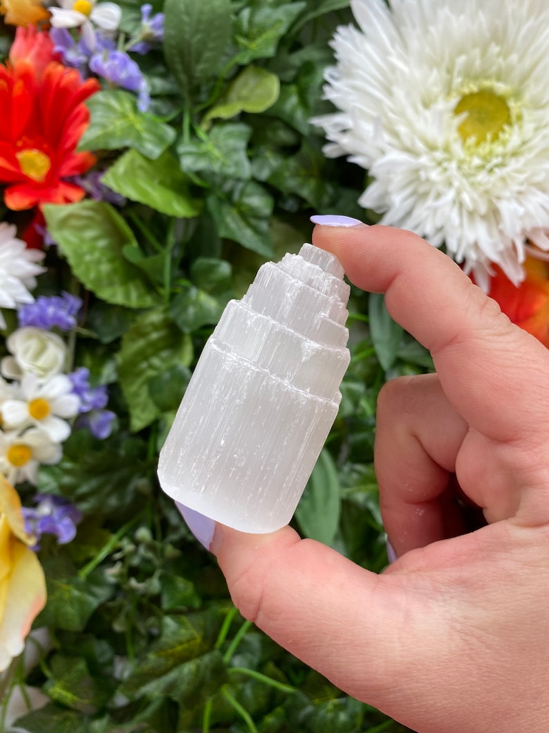 May include: White selenite crystal tower with a layered, stepped design. The crystal is smooth and polished, with a translucent white color.