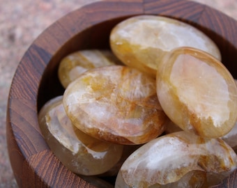 May include: A collection of smooth, oval-shaped, translucent, light brown and white stones with a hint of gold in a wooden bowl.