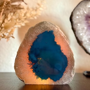 May include: A natural agate geode with a blue and orange interior. The geode is lit from within, creating a warm glow.
