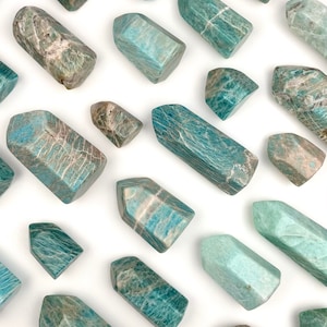 May include: A collection of green and blue amazonite crystal points. The points are various sizes and shapes, with some having a more opaque appearance and others being more translucent.