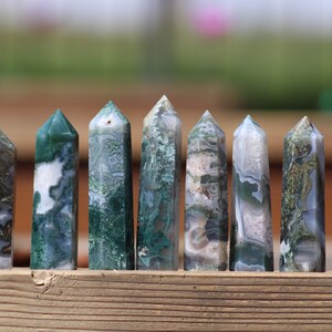 May include: A row of eight green and white agate crystal points, also known as moss agate, arranged on a wooden surface.