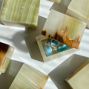 May include: A set of five green and brown onyx boxes with lids. One box is open and contains a silver ring and several blue stones.
