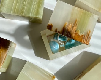 May include: A set of five green and brown onyx boxes with lids. One box is open and contains a silver ring and several blue stones.