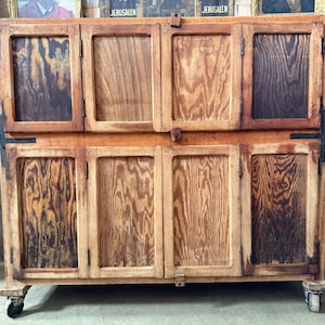 May include: An antique wooden cabinet with eight doors, each displaying a distinctive wood grain. The cabinet sits on small caster wheels and has metal hinges and latches. The wood has a warm, natural finish, typical of vintage furniture.