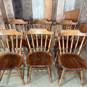 May include: A set of wooden chairs with spindle backs and seats. The chairs have a warm, reddish-brown finish, and the wood grain is visible. The chairs are arranged together, possibly for a dining set or similar use.
