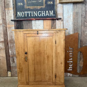 May include: A light-coloured wooden cabinet with a single door and a small brass knob. The cabinet has a rectangular shape and is made of wood. Above the cabinet is a sign that says "Trip to Jerusalem Inn Nottingham."