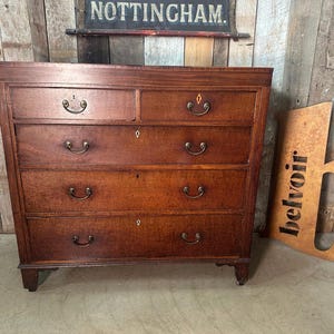 May include: A vintage wooden chest of drawers with five drawers and antique brass handles. The chest is a warm brown colour and has a classic design. The chest is a piece of furniture.