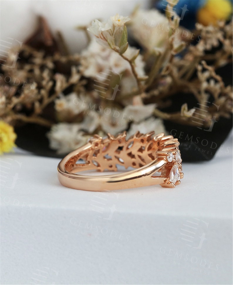 Puede incluir: Anillo de oro rosa con un delicado dise&ntilde;o calado y varias piedras claras y brillantes. El anillo presenta una fila de piedras con forma de marquesa y piedras redondas m&aacute;s peque&ntilde;as, engastadas en una banda detallada.