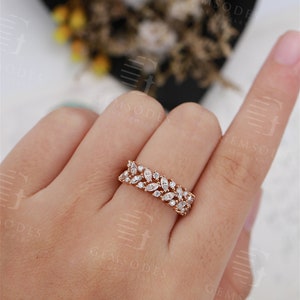 Puede incluir: Un anillo de oro rosa con una fila de piedras preciosas blancas con corte marquesa. El anillo est&aacute; engastado con m&uacute;ltiples piedras preciosas, creando un dise&ntilde;o brillante y elegante. El anillo se muestra en el dedo de una persona, destacando sus delicados detalles.