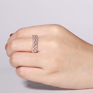 Puede incluir: Un anillo dorado con dos filas de piedras claras en forma de l&aacute;grima. El anillo se muestra en una mano, resaltando el dise&ntilde;o detallado y el brillo de las piedras preciosas. La banda del anillo tambi&eacute;n es dorada.