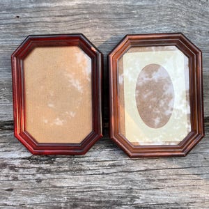 May include: Two octagonal picture frames with dark brown wooden borders and glass fronts. The left frame has a plain tan backing, while the right frame includes a cream-colored oval mat insert over a tan backing, both displaying a smooth finish.